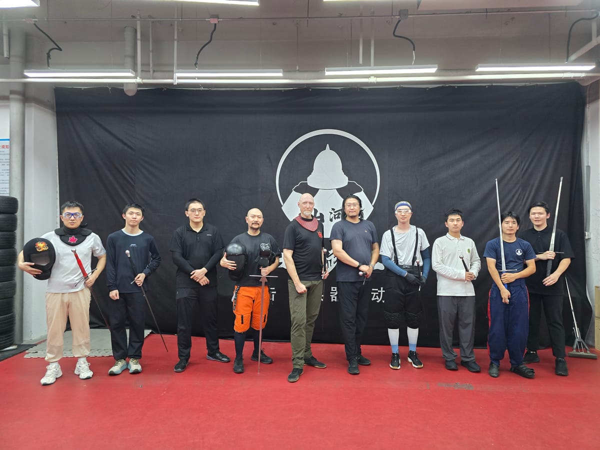 Devon Boorman with workshop participants holding swords and fencing masks at a HEMA school in Beijing
