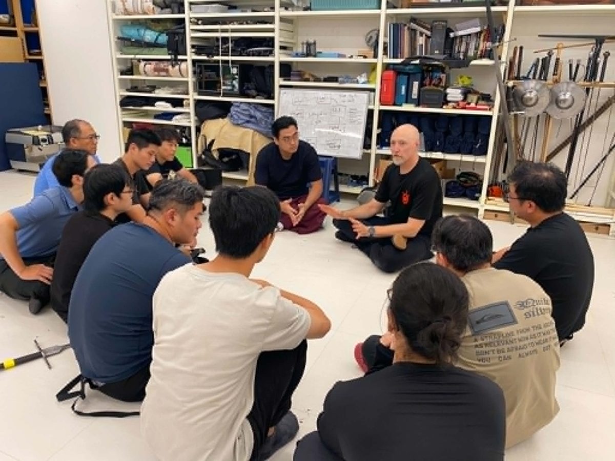 Devon Boorman leading a seated discussion circle with intensive participants on the training floor